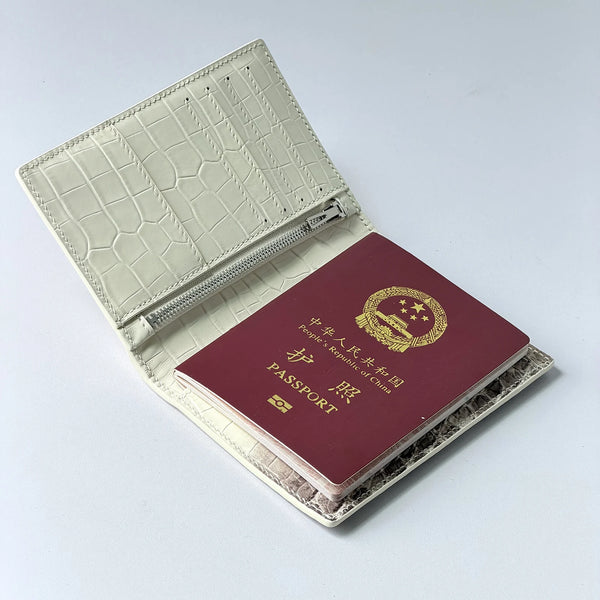 A beige leather passport holder with a crocodile pattern and a red passport inside.