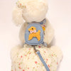 A fluffy white stuffed animal wearing a light blue dog vest with a yellow backpack and leash.