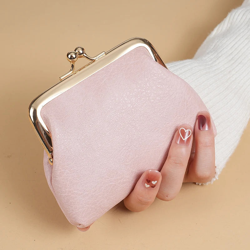 A pink velvet coin purse with a gold buckle is held by a hand against a beige background.