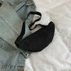 A black nylon crossbody sling bag is shown resting on a light-colored sheet next to a denim shirt.