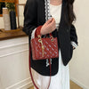 A woman holds a red textured diamond grid crossbody bag against a black blazer and white top.