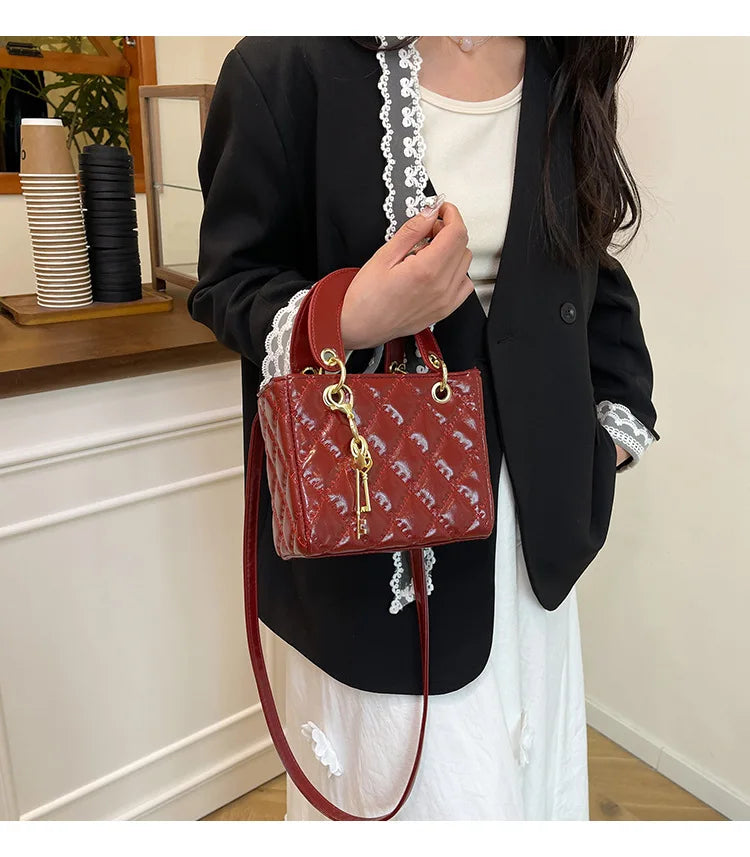 A woman holds a red textured diamond grid crossbody bag against a black blazer and white top.