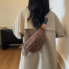 A person is holding a leopard print crossbody bag with an adjustable strap against a light beige shirt.
