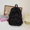 A black corduroy fashion backpack with a green and pink floral pattern resting on a white surface.