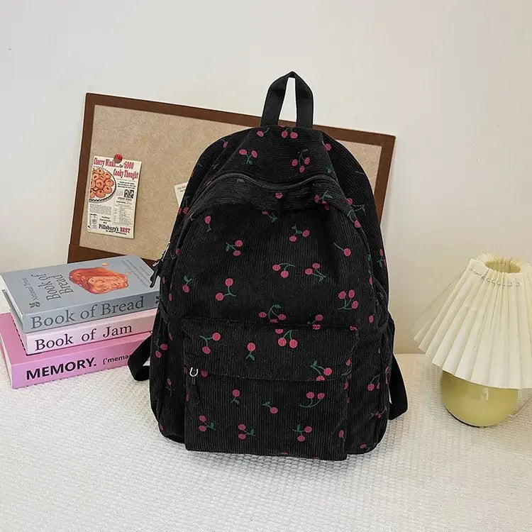 A black corduroy fashion backpack with a green and pink floral pattern resting on a white surface.