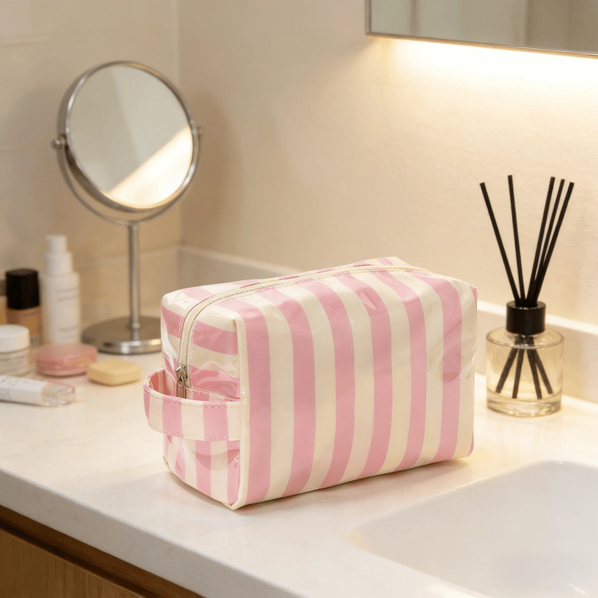 Sac de rangement cosmétique rayé rose et blanc sur un comptoir blanc à côté d'un miroir.