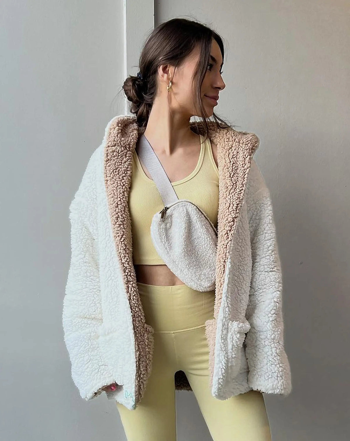 A woman wearing a yellow crop top and pants, accessorized with an ivory fleece crossbody belt bag.