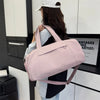 A woman holds a pink Oxford gym duffel bag with a wet/dry compartment in a modern setting.