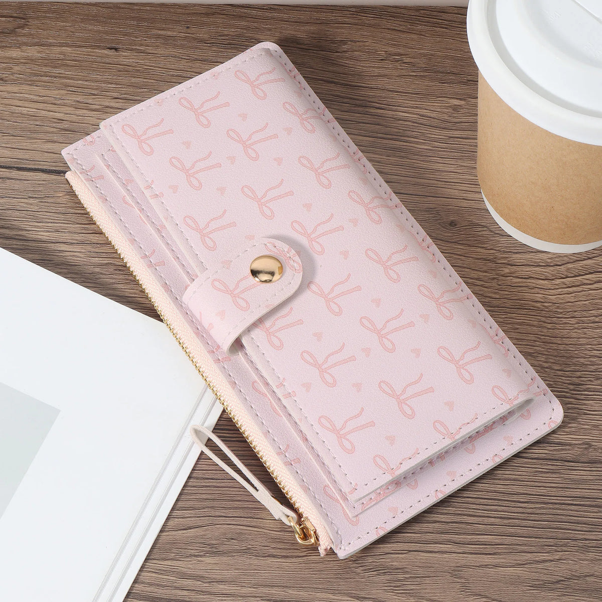 A pink elegant folding multi-card wallet with a zipper and gold hardware resting on a wooden surface.