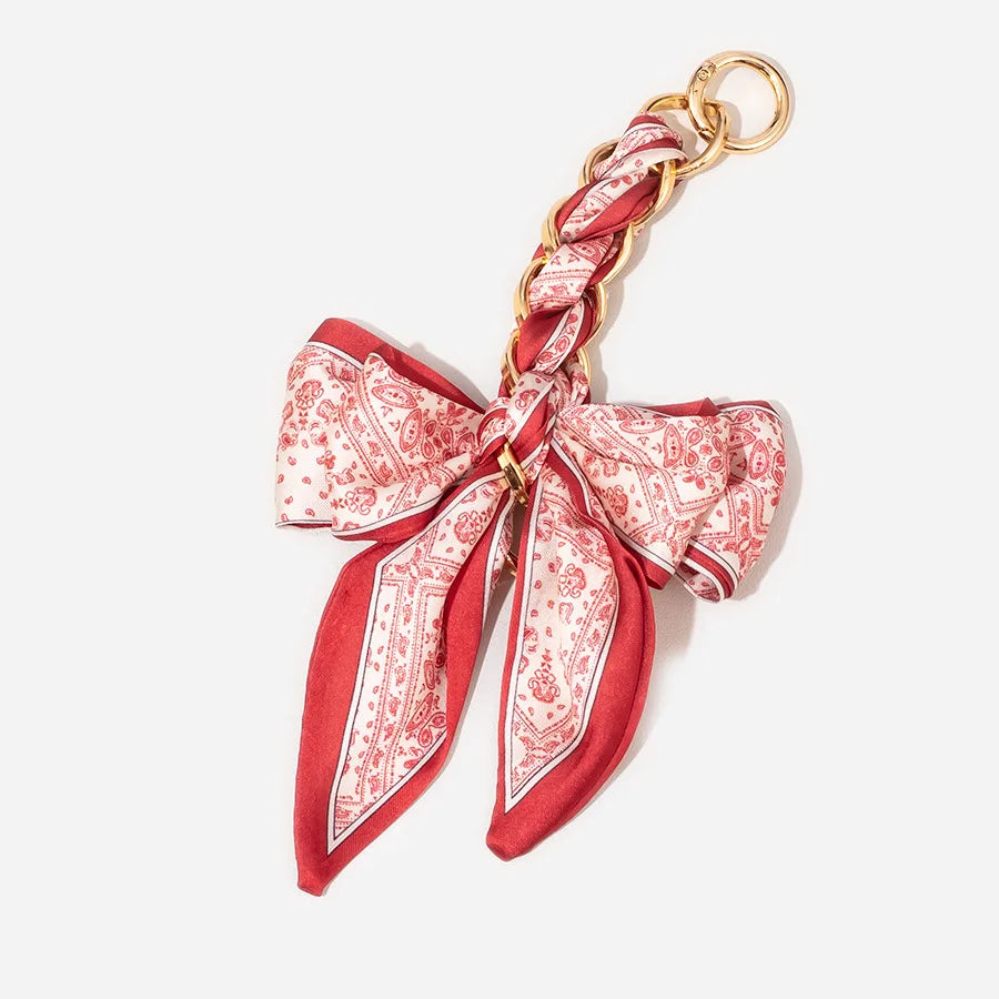 A red and white patterned fabric strap with a gold-toned clasp, designed as an adjustable bag strap.