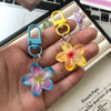 A hand holds several colorful resin flower keychains, including blue, pink, and yellow flowers.