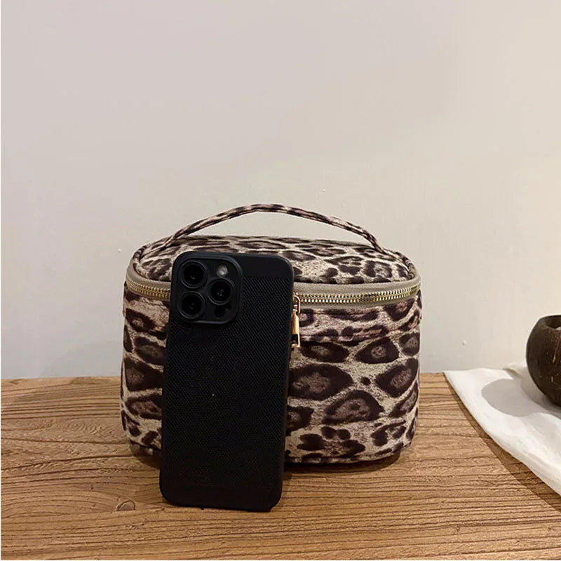A black smartphone is placed inside a leopard print faux suede cosmetic bag on a wooden surface.