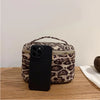 A black smartphone is placed inside a leopard print faux suede cosmetic bag on a wooden surface.