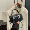 A black woven crossbody bag with a silver chain strap is displayed against a light beige jacket.