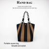 A black and tan striped square handbag with a braided strap is shown against a white background.