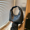 A black woven embossed hobo shoulder bag with a top handle is shown against a light-colored window blind.