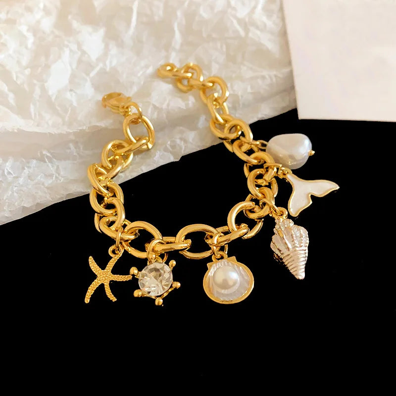 Gold chain bracelet featuring ocean pearl charms including a starfish, shell, and clam accents.