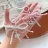 A hand holds a pink pearl keychain featuring a bowknot design and heart charms.