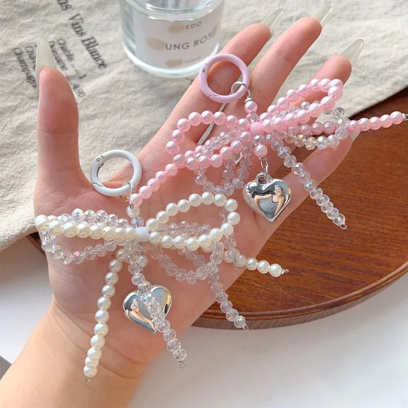 A hand holds a pink pearl keychain featuring a bowknot design and heart charms.