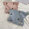 A light pink corduroy clutch bag with small brown bear embroidery resting on a white surface.