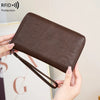 A brown leather RFID blocking travel wallet is shown being held by a hand.