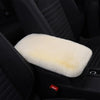 A white plush cushion is placed on a black car armrest in a dark interior setting.