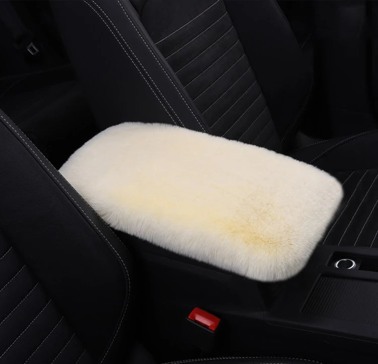 A white plush cushion is placed on a black car armrest in a dark interior setting.