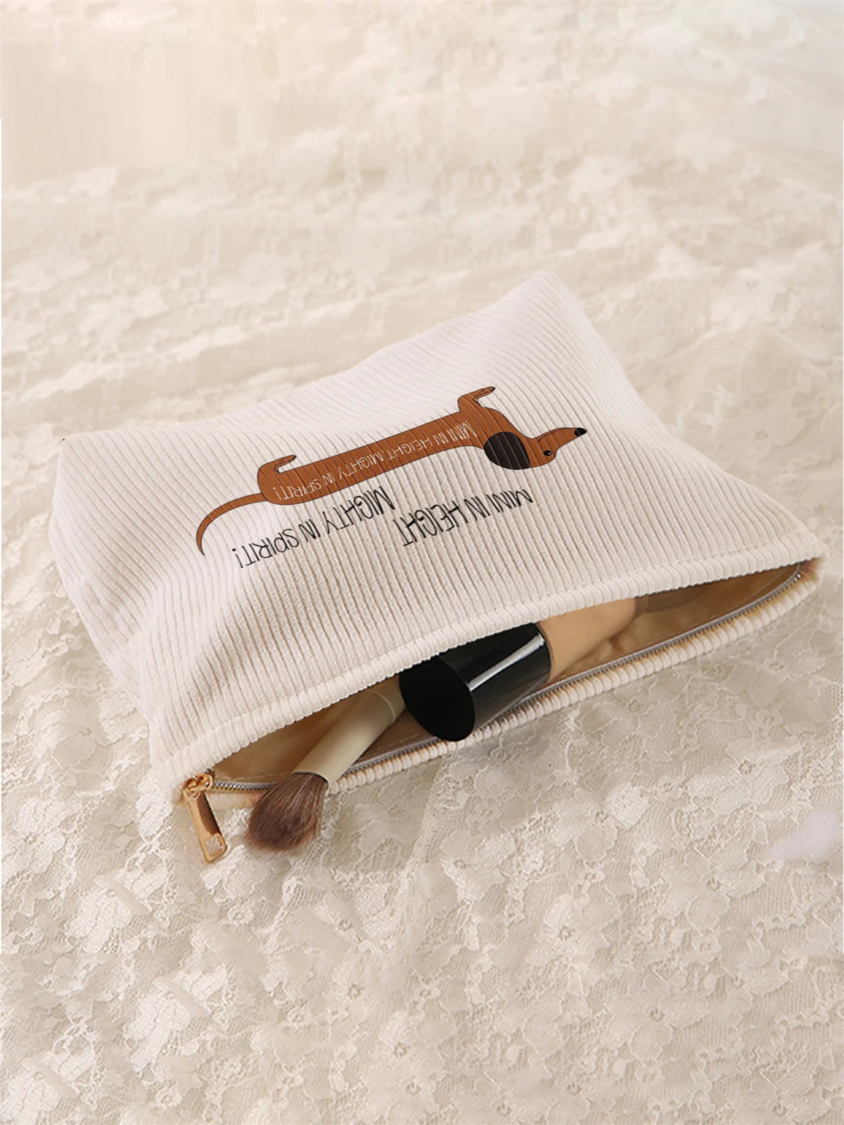 A cream-colored fabric storage bag with a brown sausage dog pattern is shown open, containing makeup brushes.