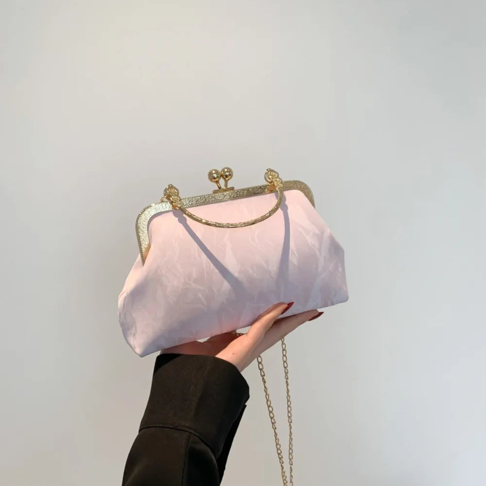 Una mano sostiene un bolso de mano de noche con lazo brillante rosa y herrajes dorados sobre un fondo blanco.