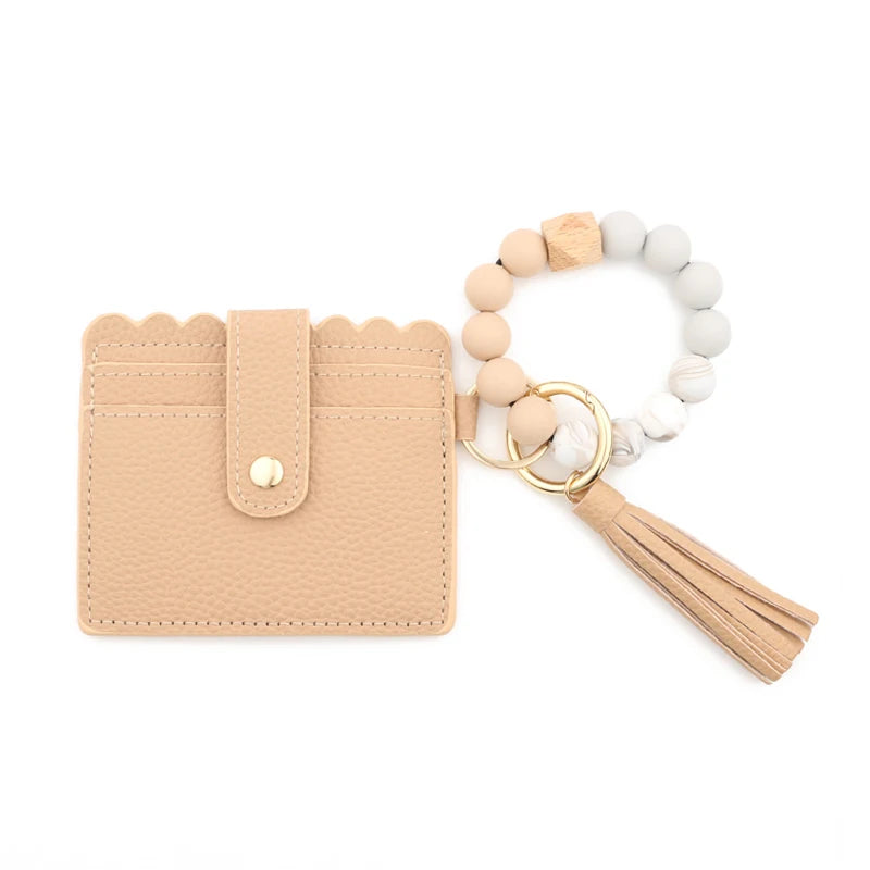A beige silicone bead bracelet is displayed next to a light tan leather card holder with a tassel.