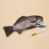 A black fish-shaped pencil case and coin purse resting on a light wooden surface next to colored pencils.