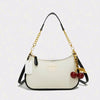 A cream-colored leather crossbody bag with a gold chain strap and dangling red fruit charms.