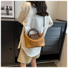 A woman is holding a tan leather crossbody handbag in front of a dark cabinet.