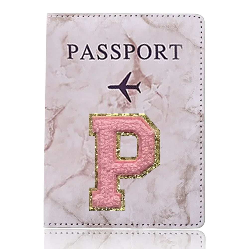 Una funda de pasaporte de imitación de cuero rosa con una inicial P dorada y un ícono de avión.