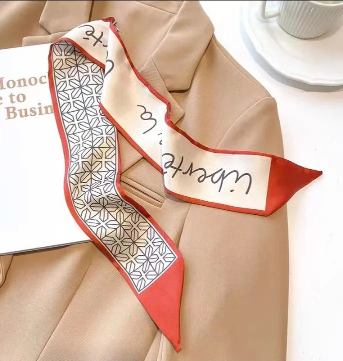 Un blazer beige présente un élégant foulard de cheveux en soie florale à motif géométrique et accents rouges.