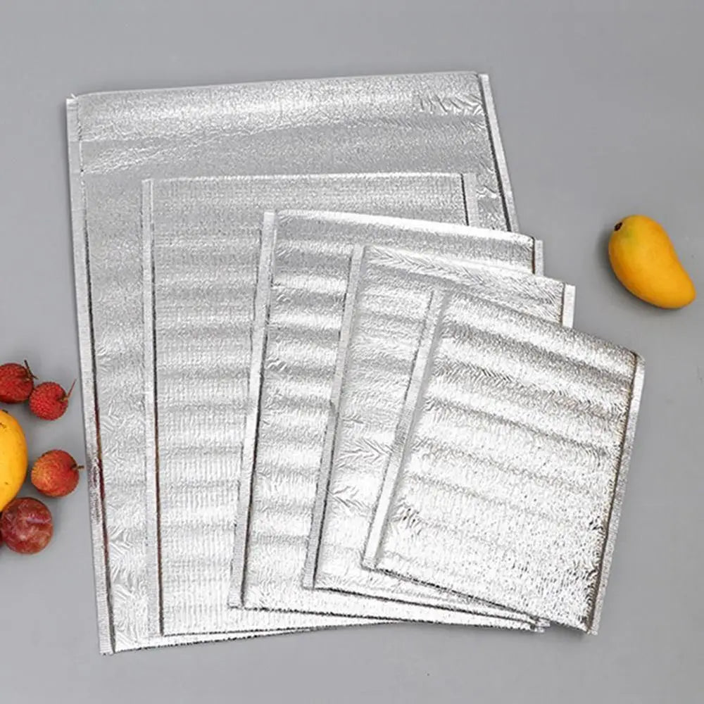Stack of silver aluminum foil insulated thermal food delivery bags with a yellow fruit.