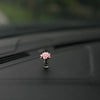 Eine kleine rosa Rosenblume in einem Glasvase auf einer dunklen Auto-Innenausstattung.