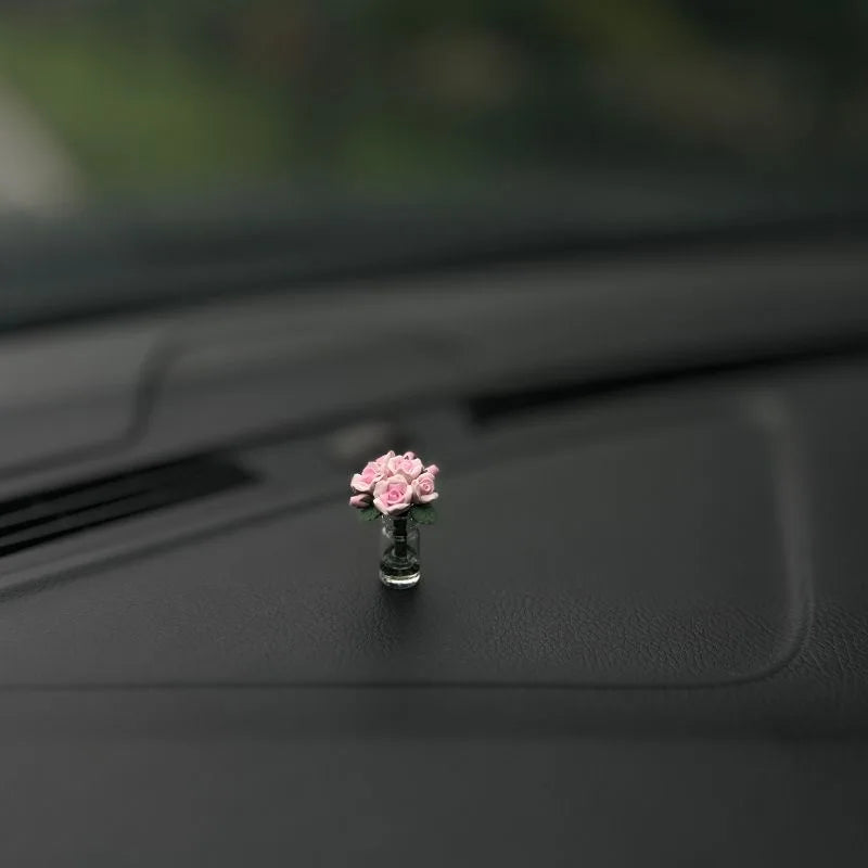 Eine kleine rosa Rosenblume in einem Glasvase auf einer dunklen Auto-Innenausstattung.