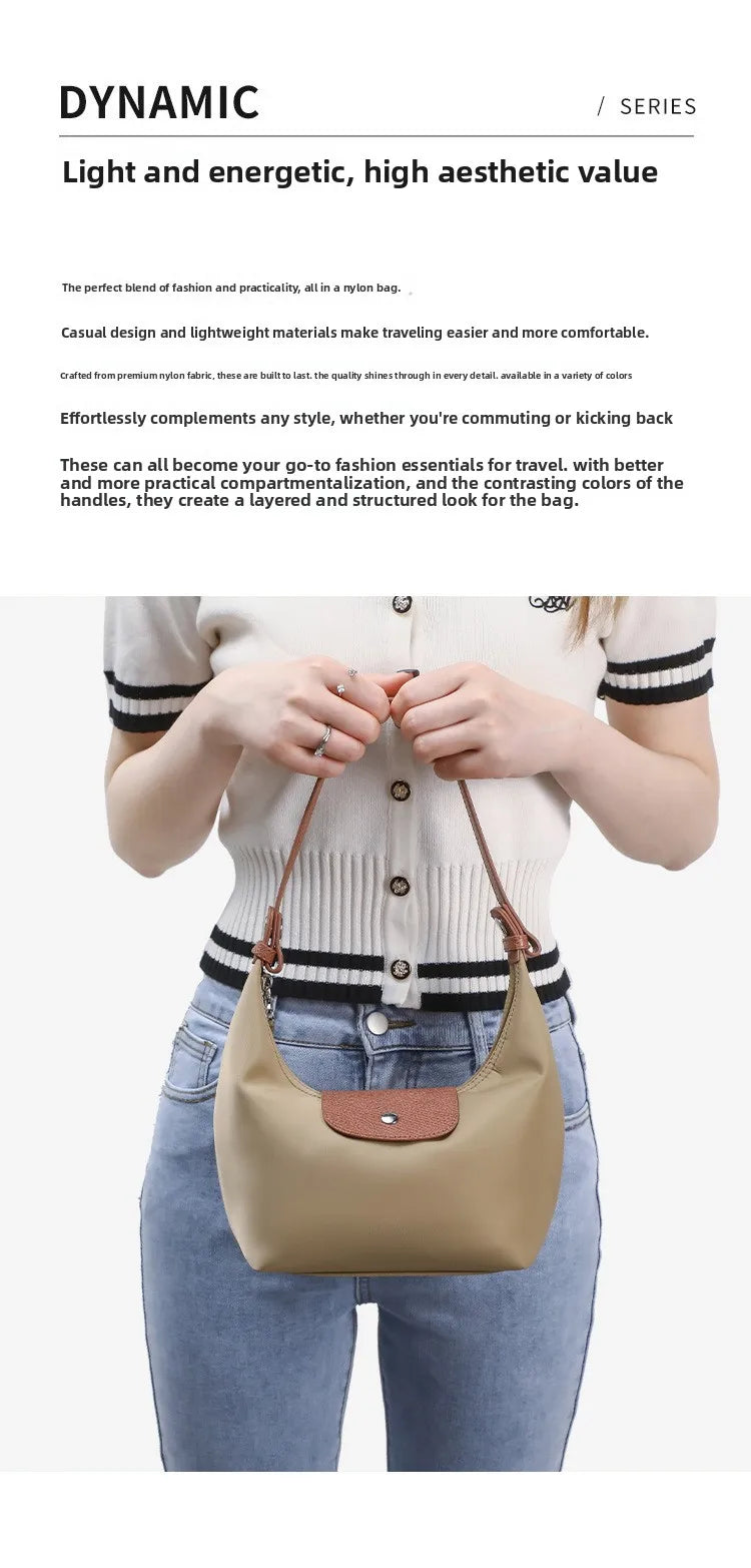 A woman holds a tan nylon dumpling crossbody bag against her torso, featuring brown leather handles and white striped top.