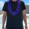 A man wearing a black t-shirt and jeans displays a purple acrylic Cuban link necklace.