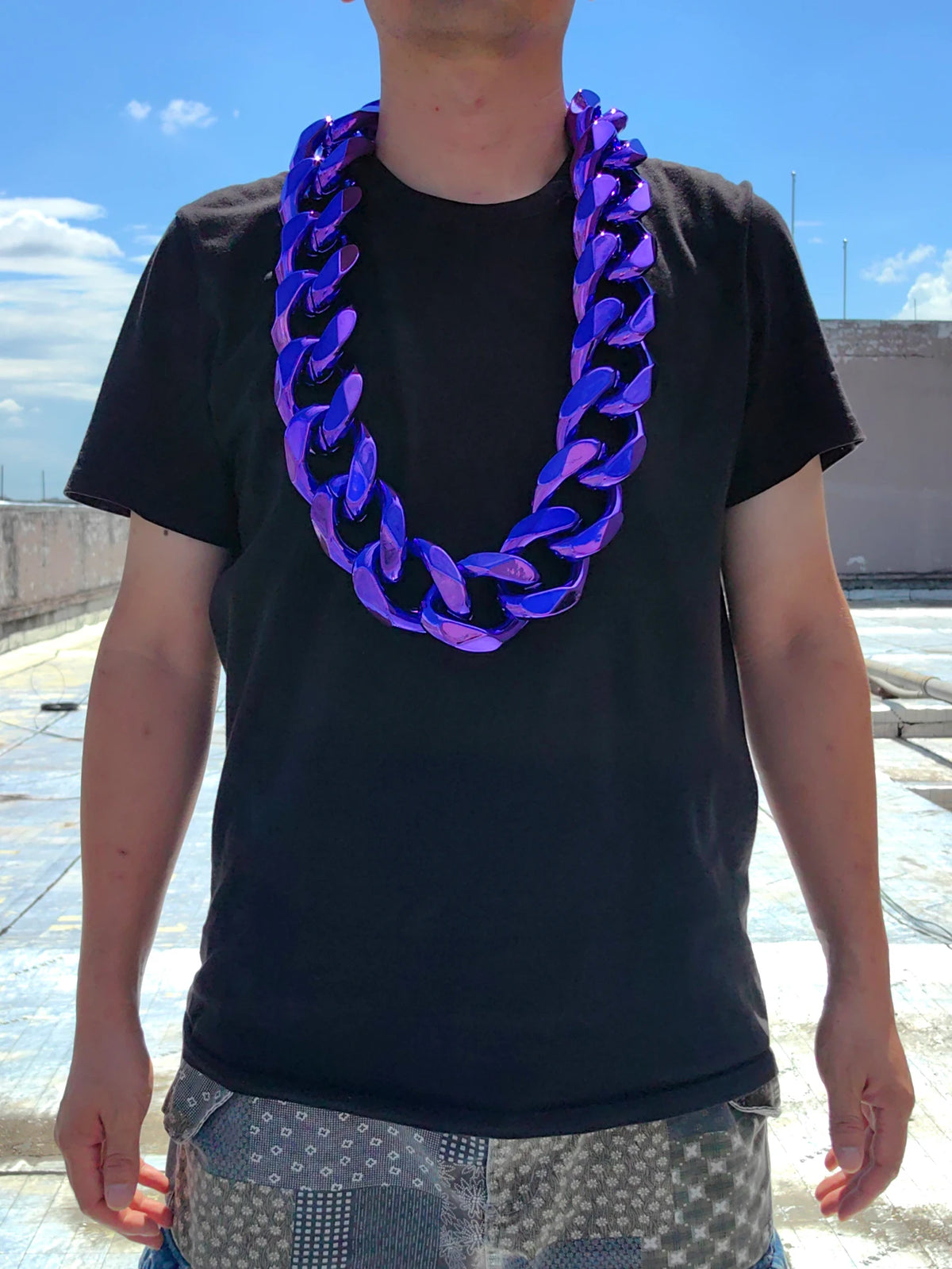 A man wearing a black t-shirt and jeans displays a purple acrylic Cuban link necklace.