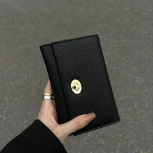 A hand holds a black compact women's card holder wallet with a gold cloud emblem.
