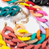 A close-up of a colorful matte acrylic choker necklace featuring interlocking rings in shades of orange, pink, yellow, green,
