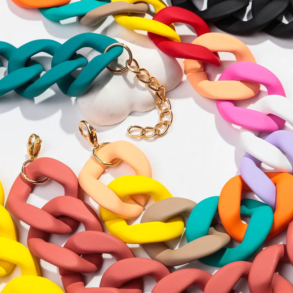 A close-up of a colorful matte acrylic choker necklace featuring interlocking rings in shades of orange, pink, yellow, green,