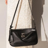 A black split leather shoulder tote bag with a silver clasp is shown hanging against a light-colored textured fabric.
