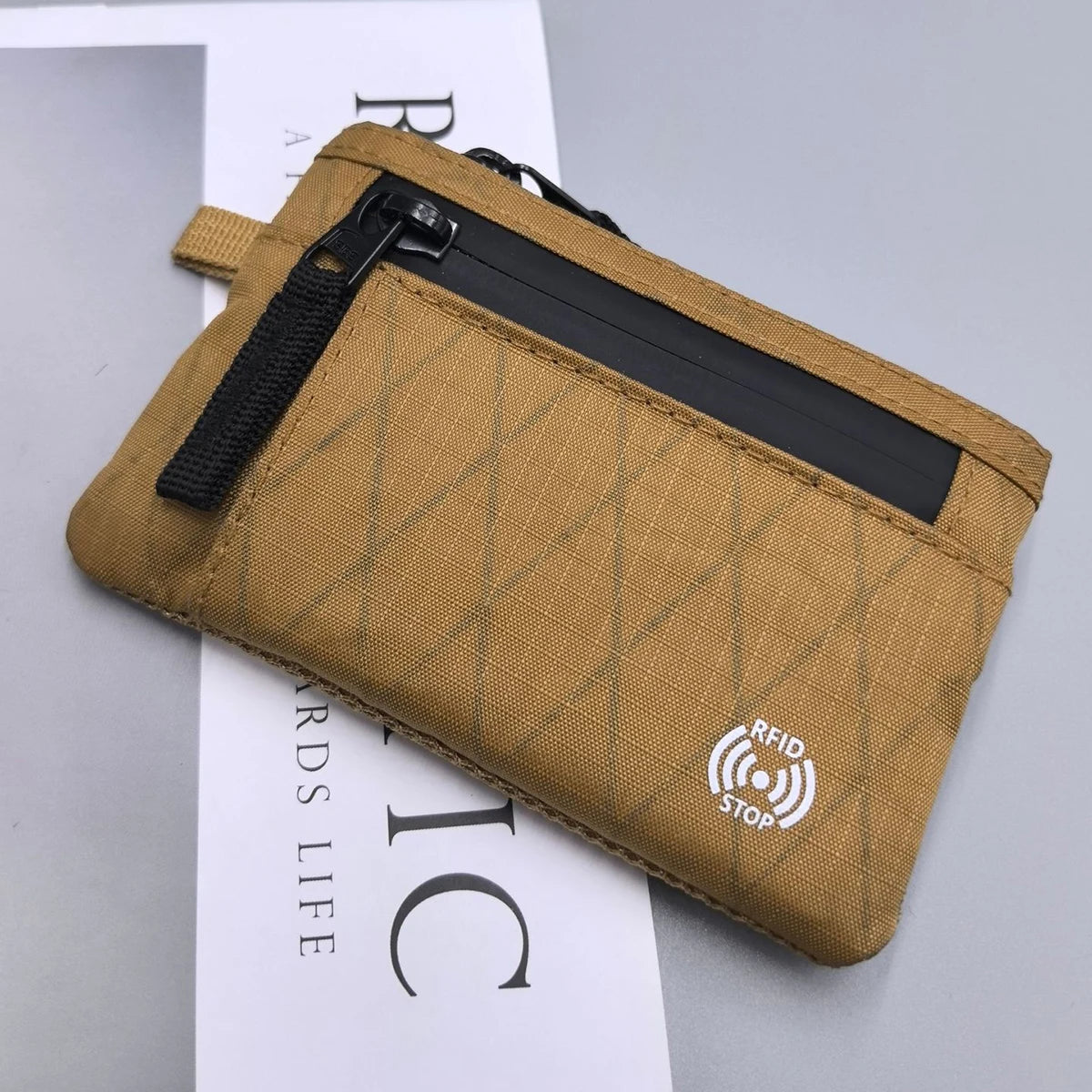 A tan RFID blocking travel wallet with a zipper and carabiner attached, shown against a white background.