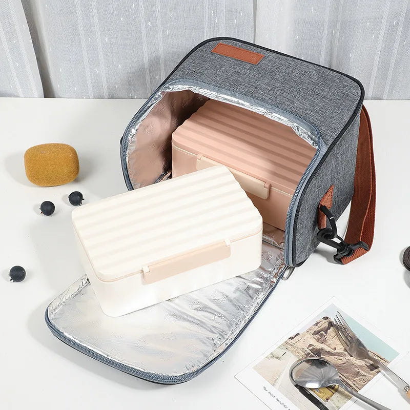 A gray insulated reusable lunch bag with a pink interior and brown strap is shown open on a white surface.
