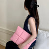 A woman is holding a pink quilted laptop sleeve on her lap.