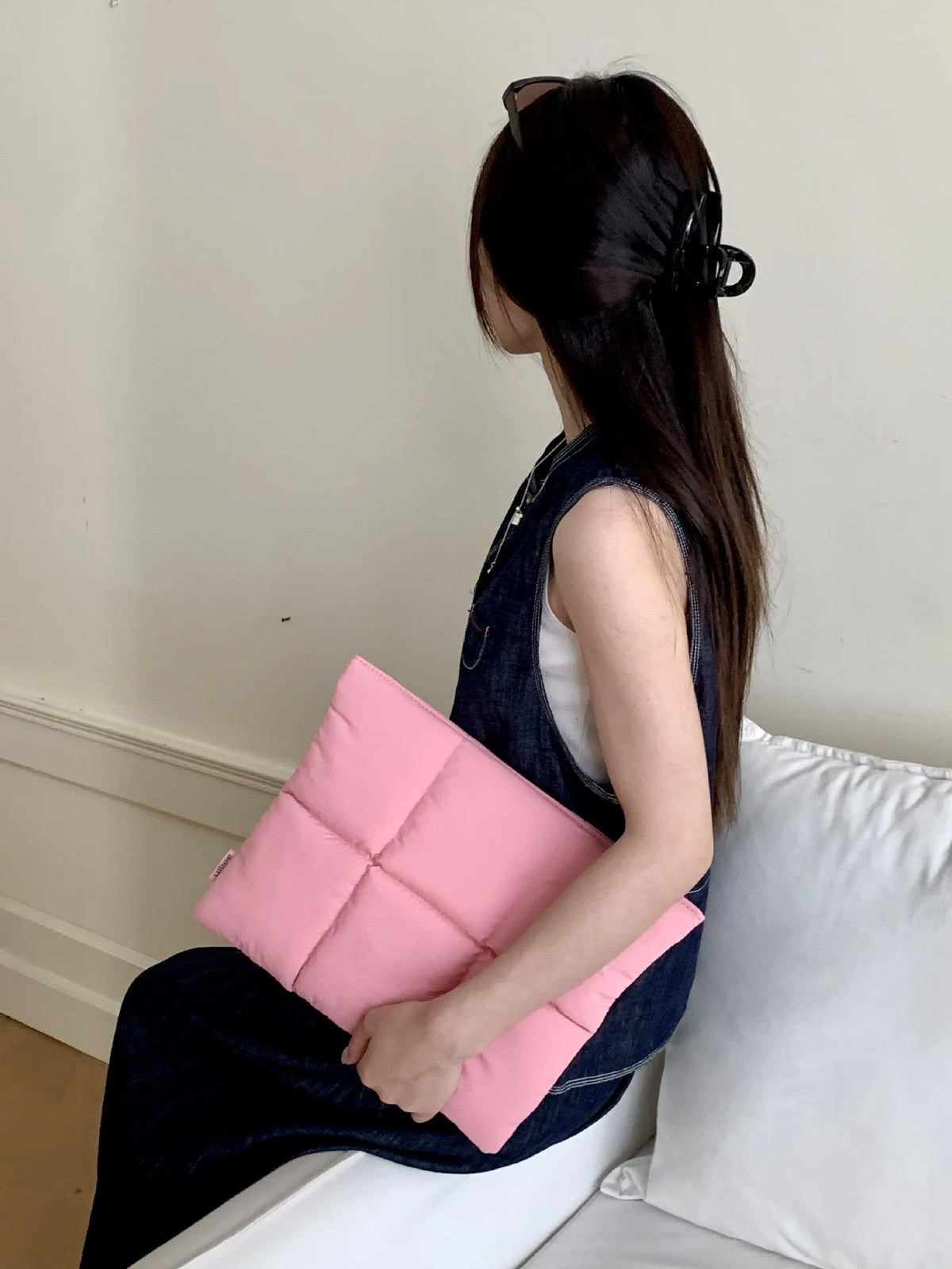 A woman is holding a pink quilted laptop sleeve on her lap.