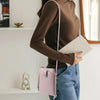 A woman wearing a brown top holds a pink compact PU leather crossbody bag and a notebook.